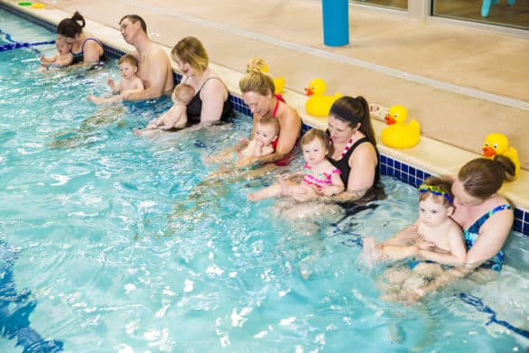 Parents with their babies at a swim class in a Goldfish Swim School pool