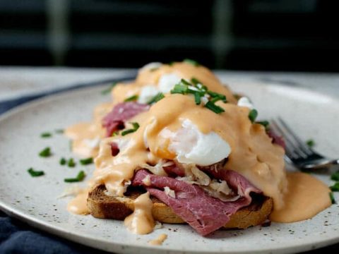 A reuben eggs Benedict topped with a thick hollandaise sauce