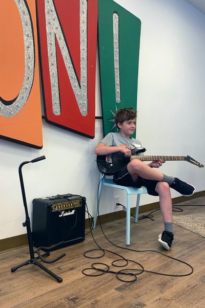 Boy strumming a guitar during a summer camp showcase at McGuigan Arts Academy