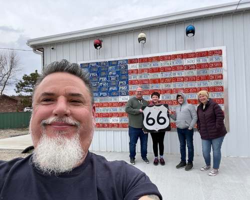 Family photo in front of an American flag made of license plate, with Aaron, the owner of Gearhead Curios,  joining in for a selfie