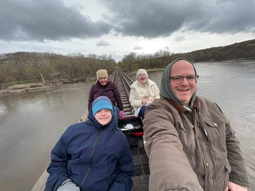 Four people in winter gear smile as they pedal over a bridge in Boone, Iowa