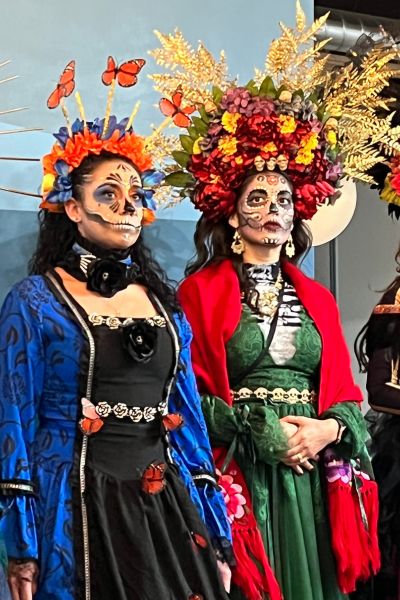 Two women in elaborate Catrina costumes pose for a picture