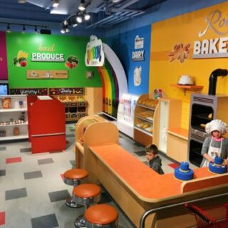 A colorful, kid-sized grocery store with one kid wearing a chef's hat in a kid bakery