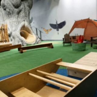 A play area inside Schramm Education Center, with green flooring, a tree with a slide in it, and a small tent in the background