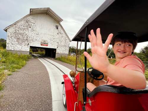 A girl waves from the driver's seat of an antique car as she drives it on a track at Vala's Pumpkin Patch and Orchard. The 