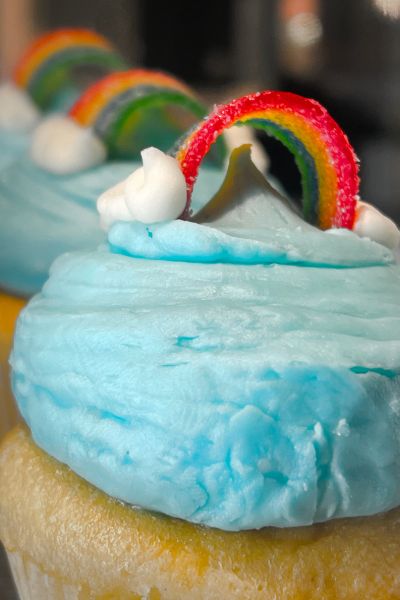 Vanilla cupcakes topped with blue frosting and candy rainbows from Jones Bros. Cupcakes
