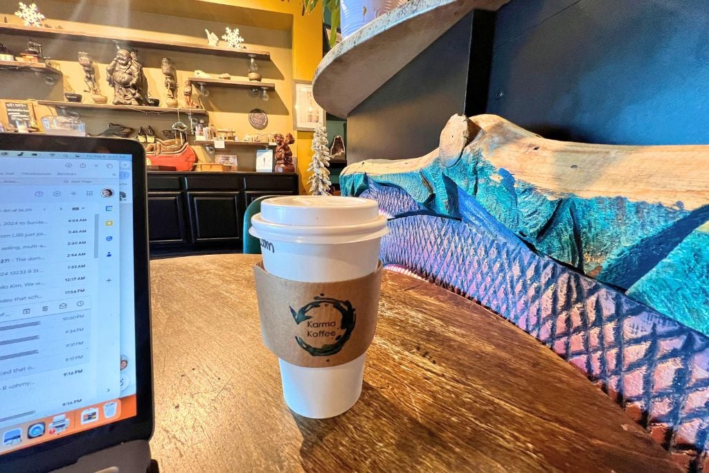A to-go cup of coffee on a table next to a brightly-colored wall at Karma Coffee