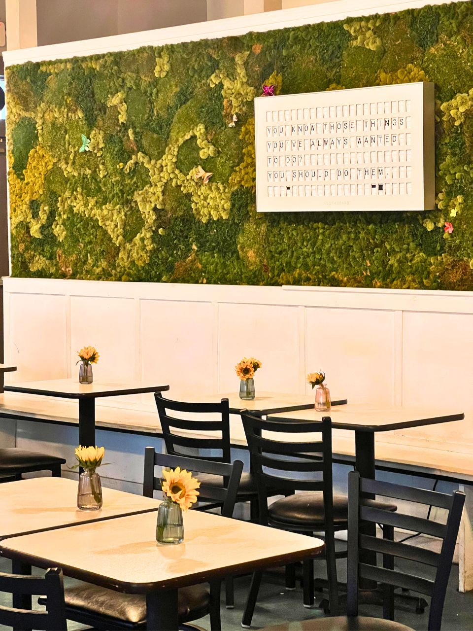The interior of Zen Coffee Co. with a green faux-plant wall and sunflowers in vases on the tables.