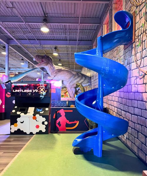 A blue slide at Prehistoric Putt, with a large T-rex replica int he background