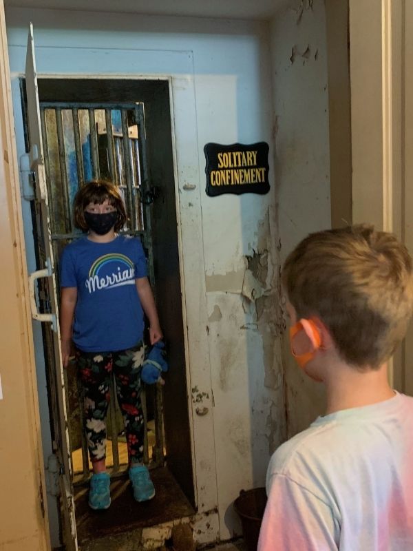 A little girl wearing a mask stands in the Solitary Confinement cell at Squirrel Cage Jail