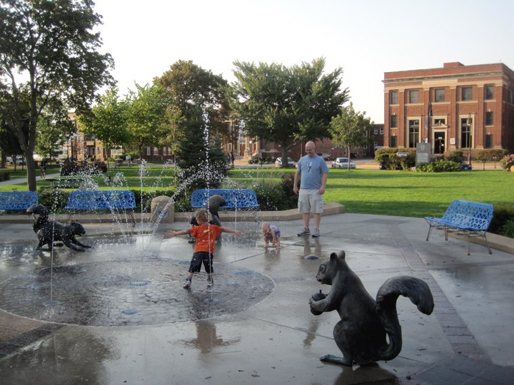 Two kids play in the spray ground at Bayliss Park while their dad watches