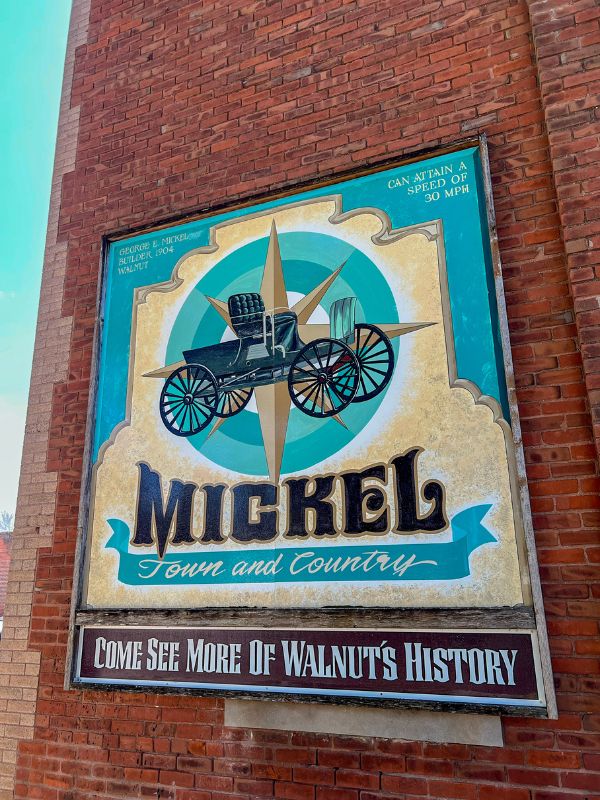 A blue and gold sign that reads "Mickel Town and Country: Come see more of Walnut's history"