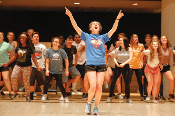 A girl sings with her hands in the air while backed by other students during the Broadway Summer Camp.